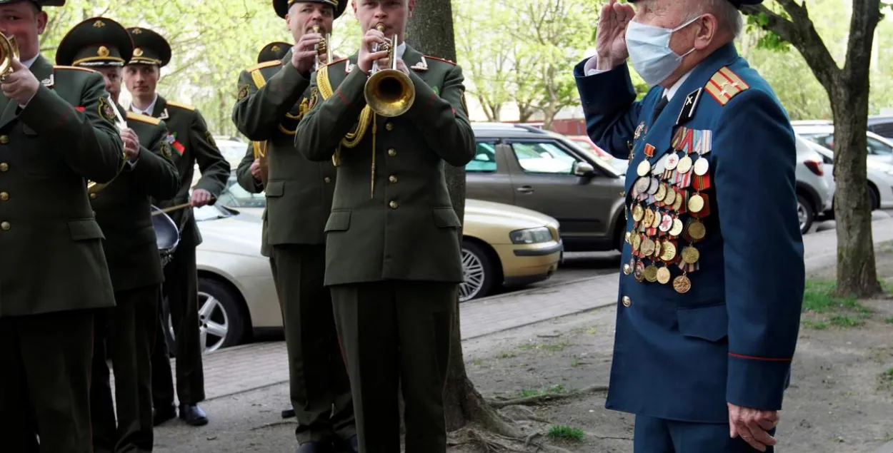 Белорусский ветеран Павел Ерошенко, надев защитную маску, слушает военный оркестр, который пришел почтить его перед Днем Победы во время эпидемии коронавируса / Reuters