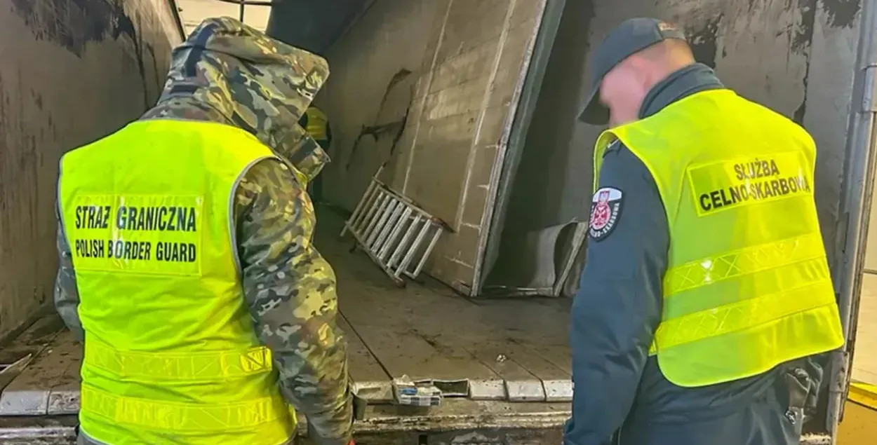 Пограничник и таможенник осматривают тайник в полу фуры
