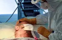 Медицинский работник утешает пациента, больного коронавирусом / Reuters