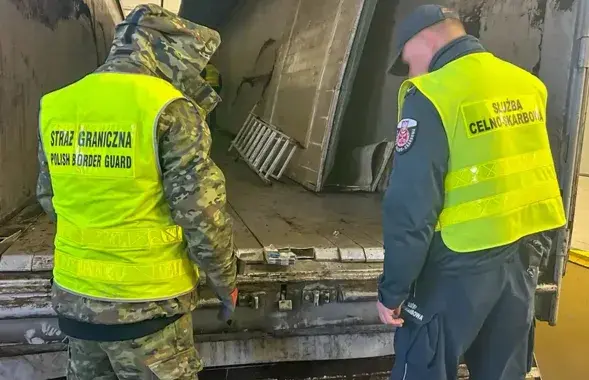 Пограничник и таможенник осматривают тайник в полу фуры
