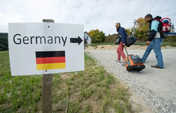 Беженцы из Сирии проходят мимо знака с надписью "Германия" и изображением немецкого национального флага возле австрийско-немецкой границы в Юльбахе, Австрия
