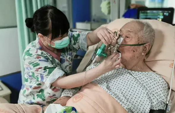 Медсестра вытирает рот госпитализированному пожилому мужчине
